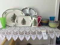 Overview of serving pieces on lace tablecloth including Spode Christmas Tree platters and jug, Royal Worcester tray, porcelain bowls, and colorful non-breakable parfait dishes.