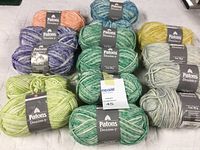 Twelve skeins of Patons Denim-y yarn in assorted variegated colors, arranged on a surface, showing the brand labels.