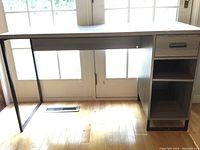 Front view of the desk showing the black metal frame legs on one side and the storage unit with drawer and open shelves on the other side.