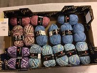 Box of various Studio Samples brand acrylic yarn skeins in multiple colors and patterns, arranged in rows inside a black tray with gold lettering.