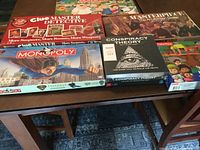 Photo of 5 boxed board games on a table including Clue Master Detective, Masterpiece, Monopoly classic, Conspiracy Theory, and Family Guy Monopoly Collector's Edition