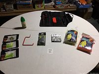 Fishing tools, Off Deep Woods insect repellent spray, red fish hook, three packages of fishing lures, earbuds, and black fishing tool roll on white table