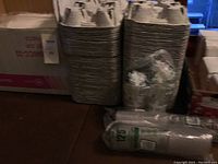 Stacks of molded fiber cardboard cup carriers next to plastic-wrapped cups and lids on floor in dim basement lighting
