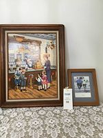 Full view of two framed prints on lace tablecloth against white wall.