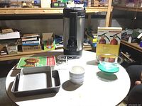 Full view of all items on round table including coffee urn, Kidde Kitchen fire extinguishers, Pyrex bowls, cake pans, ice cream cone holder and cache pot.