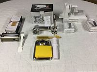 Kenome meat grinder attachment with parts and brush, Gvode pasta roller, and Urpower vegetable slicer all laid out on fabric surface.