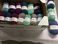 View of all 17 yarn skeins in multiple colors in a repurposed avocado cardboard box and some outside the box.