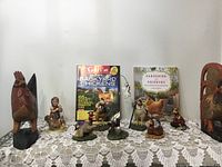 Full view of figurines, wood carvings, and books arranged on lace cloth showing size and quantity