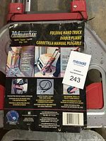Photo showing packaging of Milwaukee Folding Hand Truck with details on capacity, features, and usage including push button handle extension, elastic tie-down, and non-marking wheels.