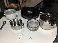 Full view of KitchenAid ice cream maker attachment, strainers, large black bowl, and stainless steel stock pot with lid on table