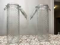 Two tall heavy pressed glass containers with textured geometric dotted pattern, hinged glass lid with metal clasp and rubber liner for airtight seal.