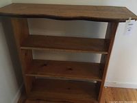 Front view of the solid wood bookcase showing three shelves and natural wavy edge on top shelf