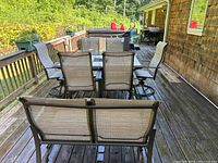 Full view of the patio set on an outdoor deck showing six chairs around a table and a loveseat bench in the foreground.