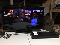 Insignia 32-inch TV and Sony DVD player placed side by side on a white surface, TV displaying a paused video, confirming functionality