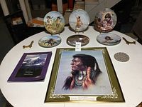 Table display with six decorative Artaffects plates, five plate stands, book, print, trivet, pottery bowl, and towel hanger visible.