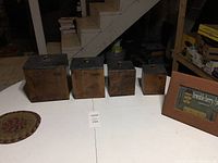 Photo displaying four wooden containers in descending size order and adjacent framed picture and woven hot plate