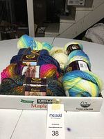 Photo showing multiple skeins of Lion Brand yarn with colorful tweed and unique ombré patterns, and off-white Caron Ice Cream yarn on white surface.