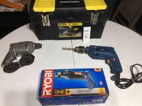 Full lot on white table: Stanley drill, Ryobi boxed speed saw with battery, and Stanley toolbox