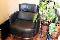 Black faux leather club chair with padded backrest and seat, steel legs and trim, minor scuffs visible on seating surface.