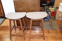 Two wooden counter stools with light grey cushioned trapezoidal seats, placed side by side.