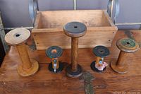 Photo showing wooden basket with metal handles and five wooden and metal spools of various sizes arranged in front of it