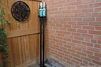 Two black Bernzomatic patio torches standing upright in an outdoor corner near a wooden fence and brick wall