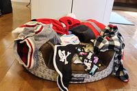 Image showing the Kirkland pet bed with various small pet outfits and accessories arranged on and around it, including hats, scarves, and a squeaky moose toy.