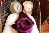 Photo showing all three hats on a chair: maroon Berlin hat in front, two other hats behind, one beige Lee hat and one cream Tilley hat