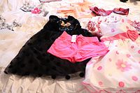 Lot of little girl dresses and pink shorts arranged on a bed, showing various colors and some with floral and Minnie Mouse designs.