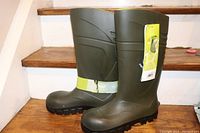 Side and front view of two Bekina Steplite safety boots on stairs, showing intact tags and label, dark green color, rugged soles and mid-calf height.