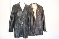 Two men's leather jackets on hangers, one black and one dark brown, showing full front view and detail of style.