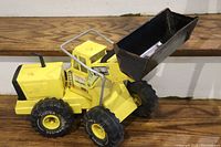 Yellow metal Tonka shovel truck with large black bucket lifted, front-side view.