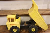 Side view of the large yellow metal Tonka dump truck showing liftable dump bed, metal construction, and broken plastic windows in the cab.