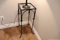 Full view of the metal and glass table stand placed next to a wall with a lamp base on top.