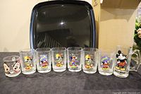 Front view showing all 8 glasses and mugs arranged on table with black tray and box behind.