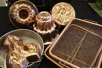 Four copper-colored decorative molds with varied shapes, one gray round springform pan inside the springform pan a reusable baking parchment and two rectangular baking trays.