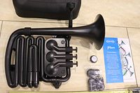 Nuvo Brass jHorn black model disassembled alongside carrying case, valve grease, booklet, and 3 C tubes for tuning.