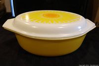 Full view of the yellow Pyrex casserole dish with the lid on, showing the sunflower daisy design on top and the yellow base.