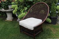 Rattan chair outdoors on grass with white cushion showing front and side profile.