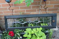 Front view of stained glass window panel showing textured glass with diamond-shaped leaded patterns and hanging chains. Framed in black wood.