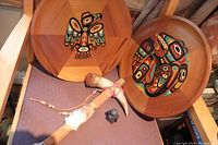 Photo showing two round red cedar trays with Indigenous painted designs, an Indigenous tomahawk with suede straps, and a small penguin figurine.