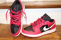 Side view of women's Air Jordan shoes showing black and red colorway, red laces, and white Nike swoosh on the outside.