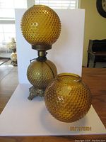 Front view of amber hobnail glass globe lamp with metal decorative base and extra matching globe placed in front