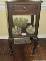 Front view of antique bedside table with glass bowls on lower shelf. Shows drawer and cabriole legs with claw feet.