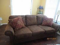 Front view showing the brown 3-seat Broyhill sofa with three cushions and two patterned throw pillows against a window.