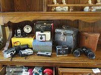 Overview photo showing all cameras, boxes, binoculars, and cases displayed on a wooden shelf.