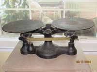 Front view of antique black cast iron Detecto balance scale with two round weighing pans on either side.