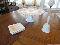 Overview photo showing all three items: pedestal dessert plate, bell, and trinket dish on wooden table with vintage lamps in background