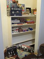 Shelf containing boxed games including Texas Hold 'Em poker set, Sequence, Buzz Word, multiple decks of cards, Monopoly, The Price is Right, and Beatles Trivia Pursuit