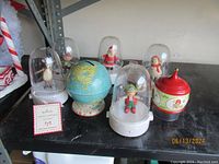 Five Hallmark Happy Tappers under plastic domes with base, along with vintage tin globe bank and holiday tin container on shelf.
